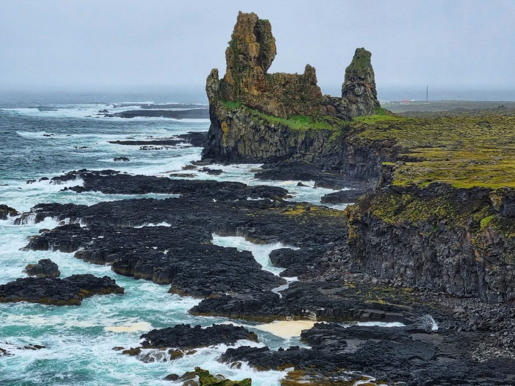 brown and green rock formation on sea during daytime